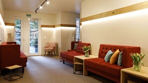 A modern lobby with red sofas, a wooden coffee table, and a small side table with a vase of flowers. - Casa Palatina Vinotel (Grosskarlbach)