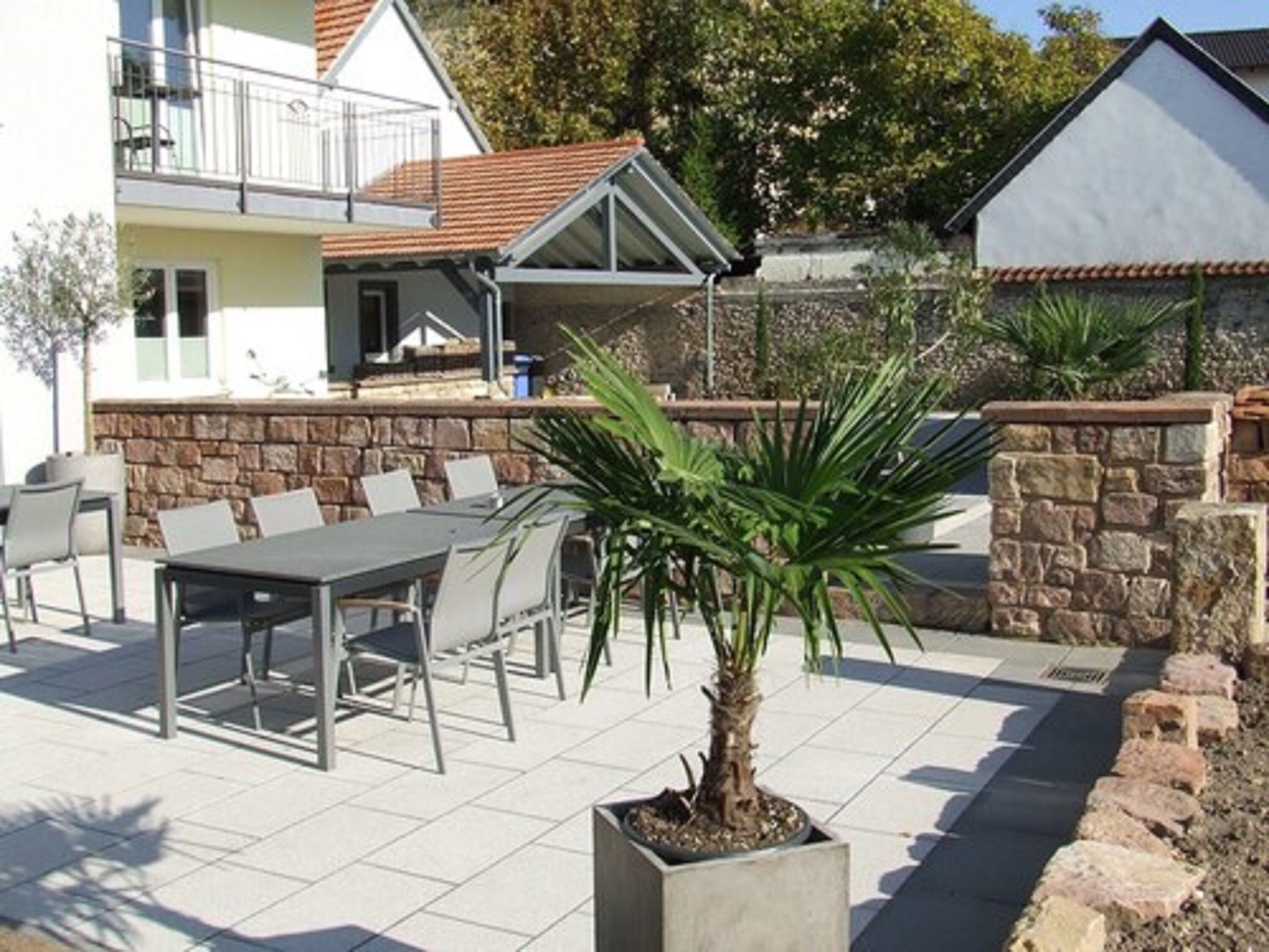 An outdoor patio with a table and chairs, a potted plant, and a stone wall.