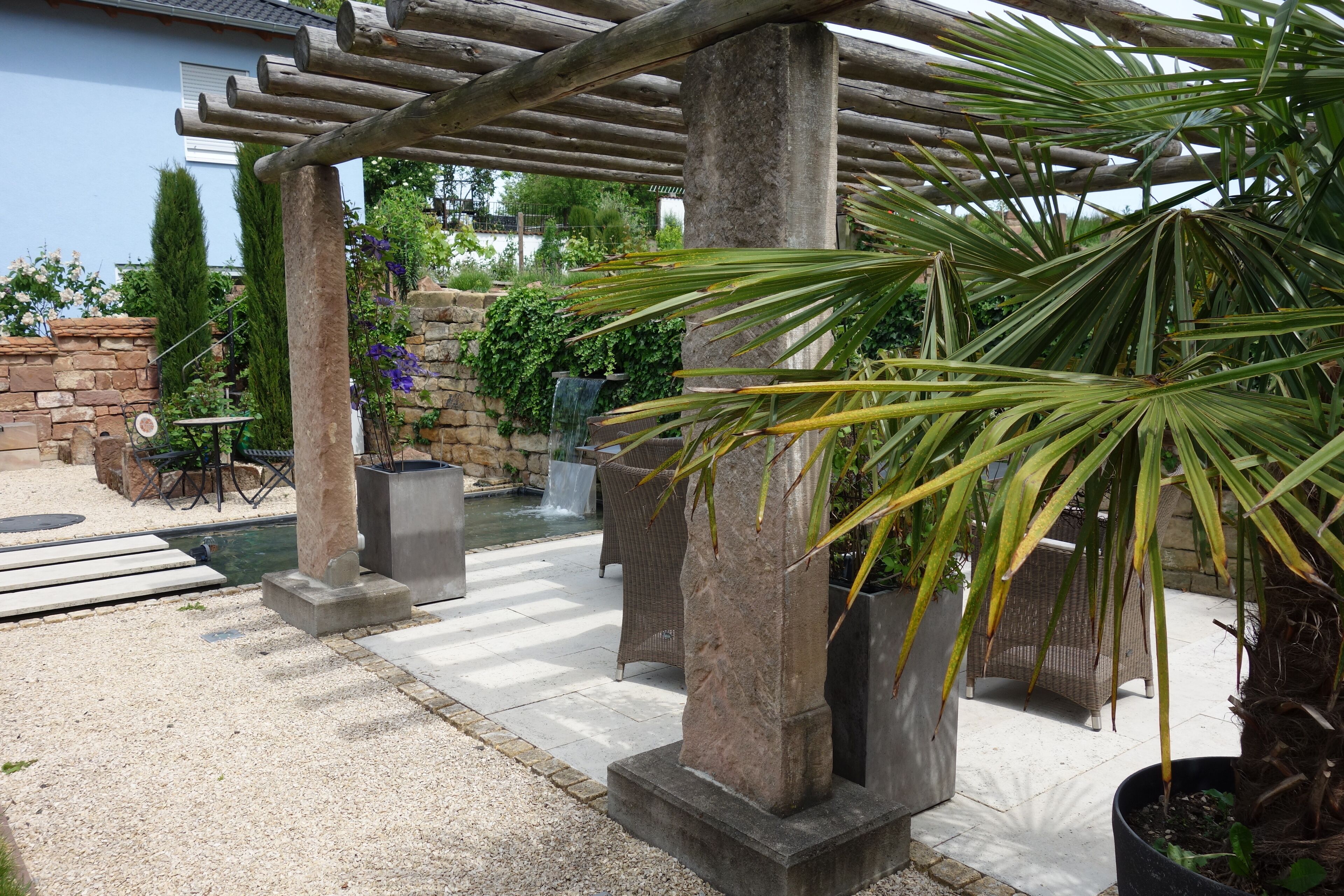 Un área de patio techada con pilares de piedra, una pérgola y plantas en macetas.