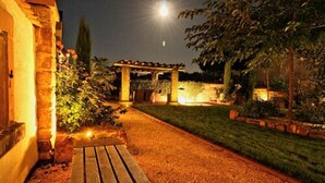 A well-lit outdoor area with a wooden bench, a stone pathway, and a pergola. - Casa Palatina Vinotel (Grosskarlbach)
