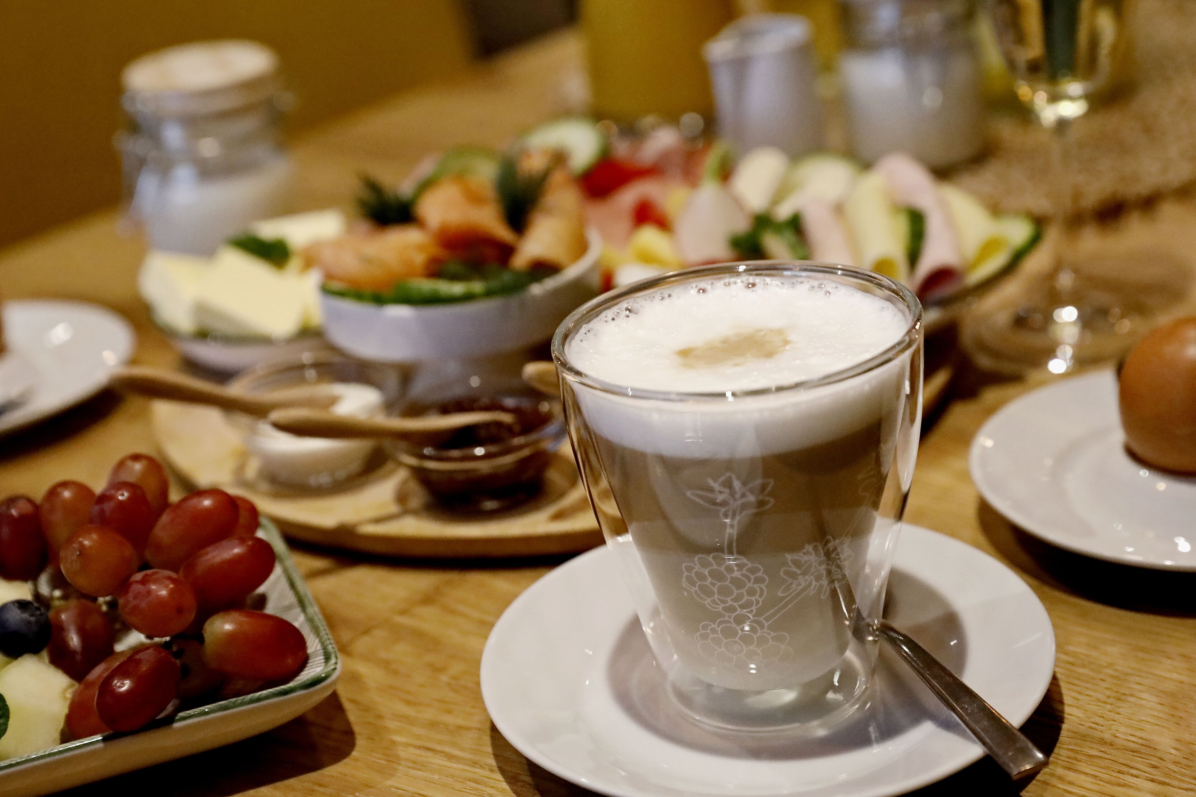 Une table à manger avec une tasse de café, une assiette de raisins et un saladier de salade.