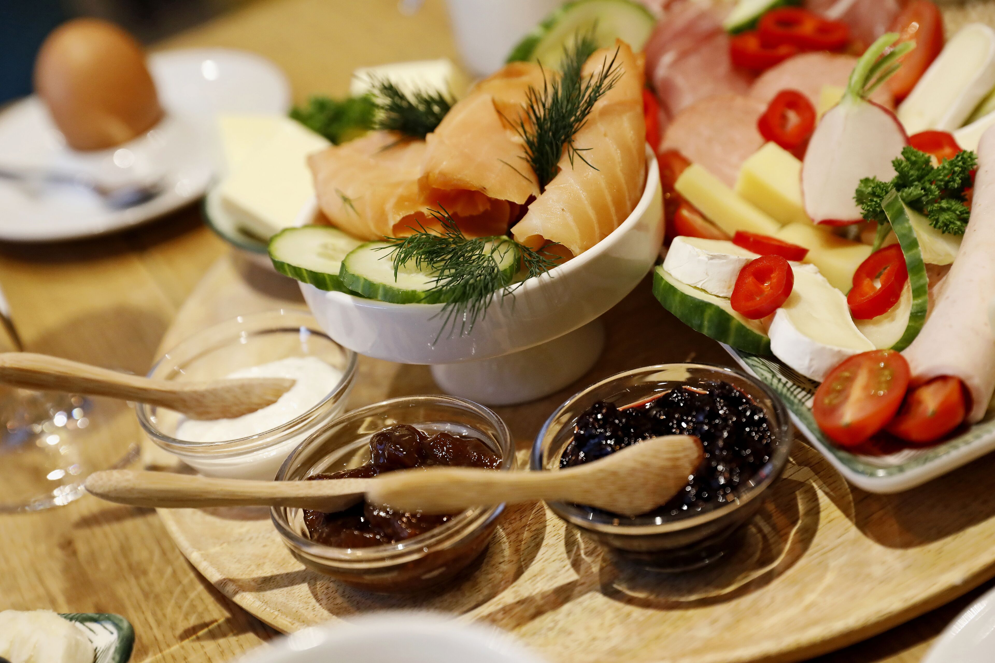A variety of food items including smoked salmon, cheese, and vegetables on a wooden table.