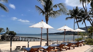 A beachside lounge area with wooden loungers and white umbrellas, a pool, and a view of the sea. - Pearl of Samui Resort (Koh Samui)
