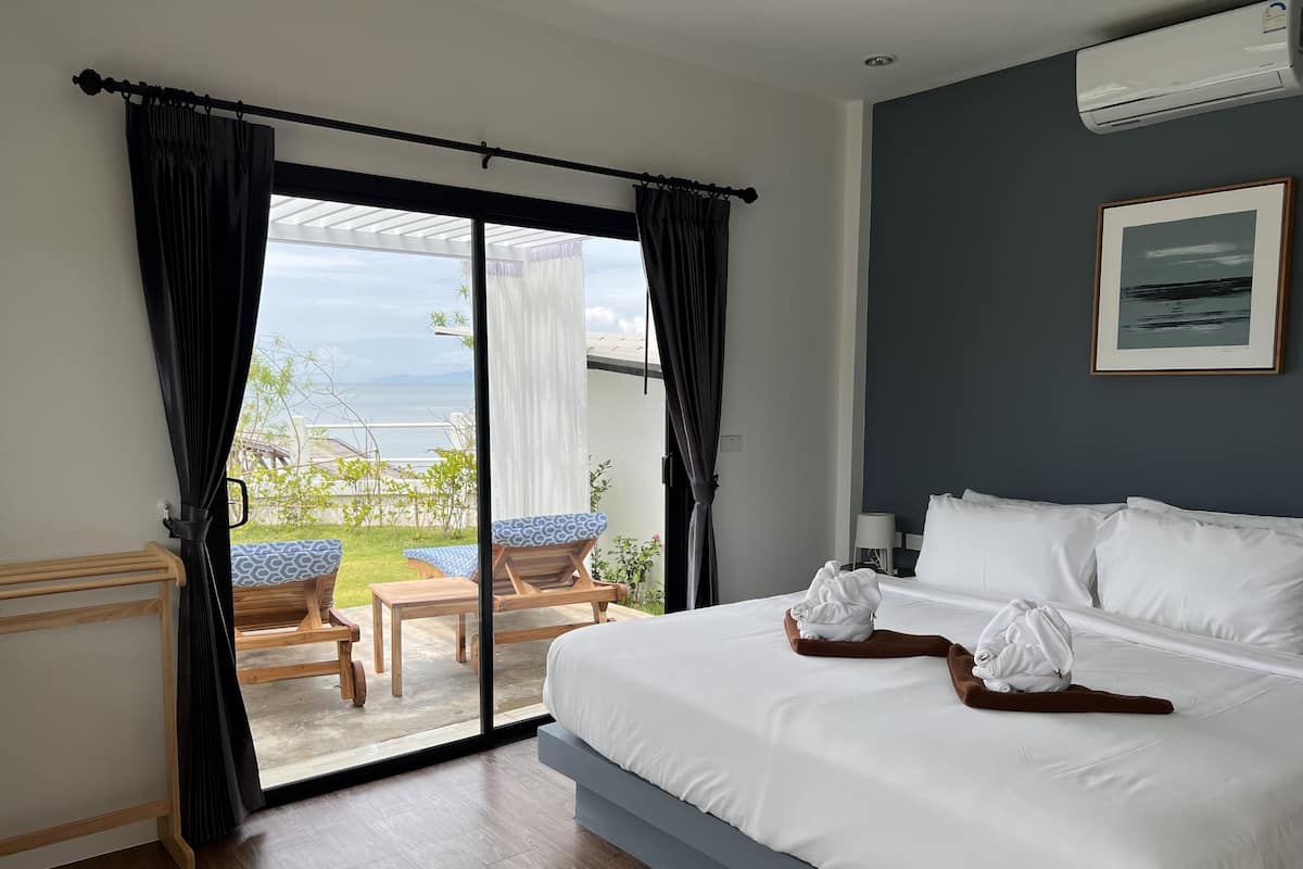 A hotel room with a large bed, a view of the sea, and a balcony with chairs and a table.