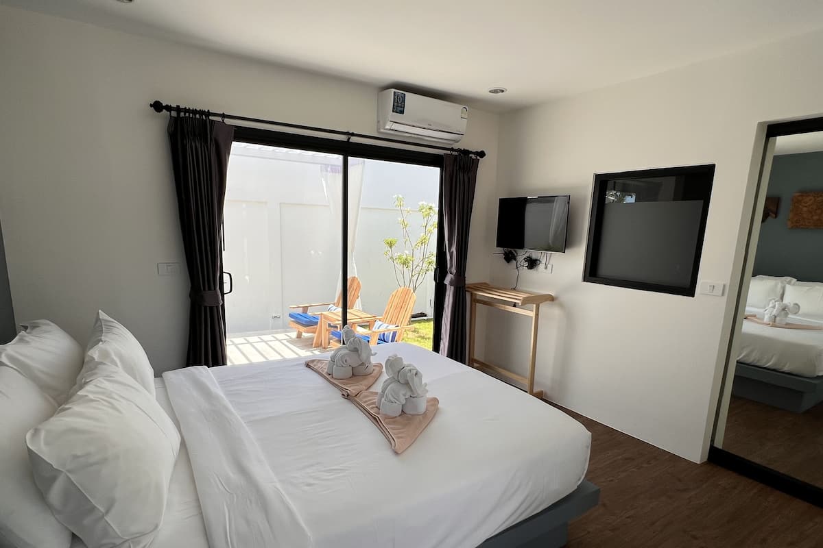 A hotel room with a bed, a TV, an air conditioning unit, and a view of the outside.