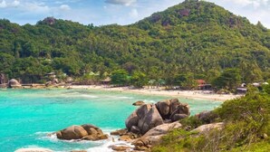 A coastal landscape with a beach, clear turquoise waters, and a forested hill in the background. - Pearl of Samui Resort (Koh Samui)