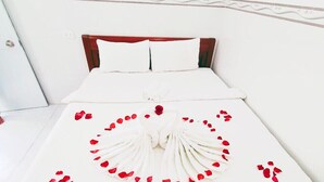 A neatly made bed with white linens, a wooden headboard, and a decorative arrangement of rose petals and a single rose on the bedspread.