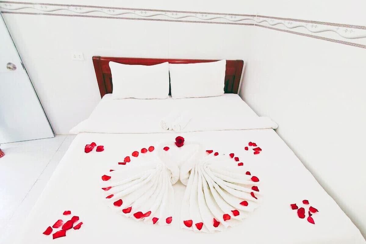 A neatly made bed with white linens, a wooden headboard, and a decorative arrangement of rose petals and a single rose on the bedspread.