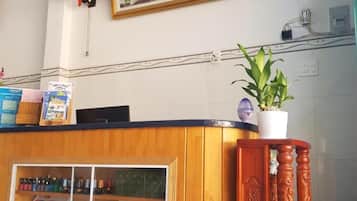 Een receptiebalie met een ingelijste afbeelding erboven, een houten toonbank en een kamerplant.