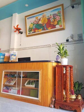 A reception desk with a framed artwork above, a wooden counter, and a potted plant.