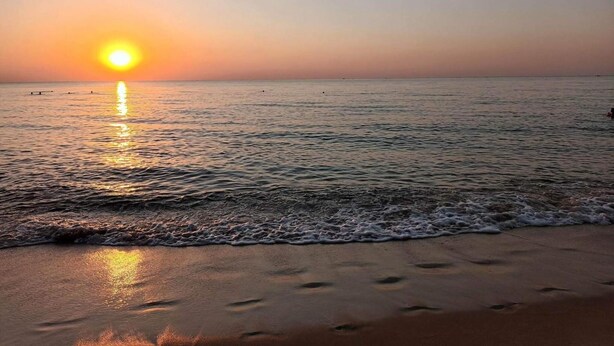A beach at sunset with calm waters and footprints in the sand.
