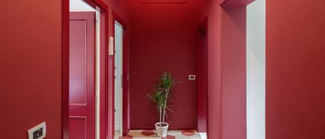 Un pasillo con paredes rojas y un suelo de patrón geométrico, que conduce a una puerta con una planta en maceta en el centro.