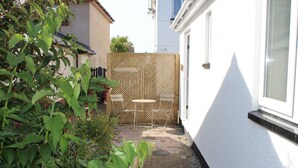 A small outdoor patio with a wooden table and chairs, surrounded by a white wall and a lattice fence. - Thistledene (Braunton)