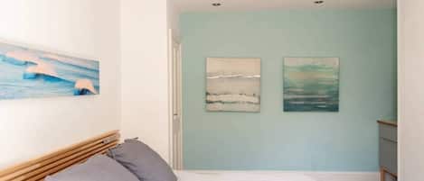 A bedroom with a bed, a wooden headboard, and two wall-mounted paintings.