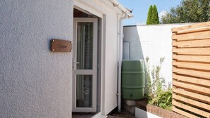 A house entrance with a door labeled "Copper," a green water tank, and a wooden fence. - Thistledene (Braunton)