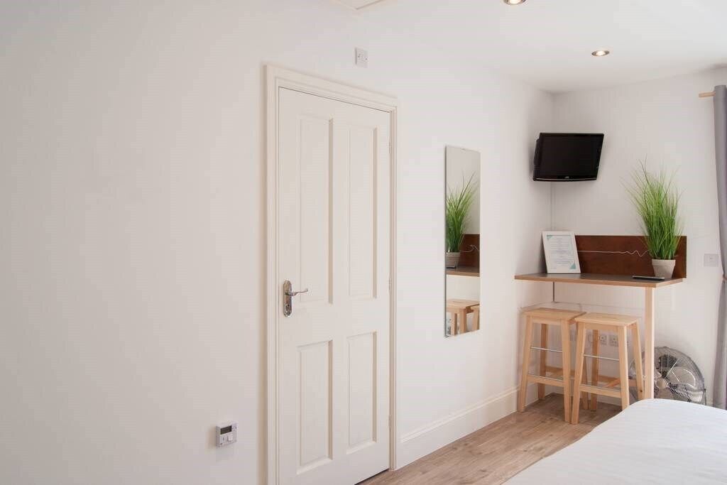 A bedroom with a bed, a desk with a chair, a TV mounted on the wall, and a door.
