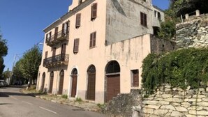 Um edifício de dois andares com varanda no segundo andar, janelas em arco e uma parede de pedra em primeiro plano.