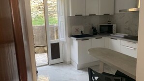 Cozinha com armários brancos, micro-ondas e pia. Há uma porta que dá para uma área externa.