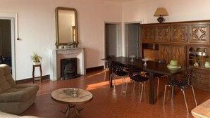 Uma sala de estar com lareira, uma mesa de jantar com cadeiras, um sofá e um armário com portas de vidro.