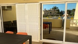 En udendørs patio med et bord og stole, en skydedør der fører til en balkon, og udsigt over de omkringliggende bygninger.