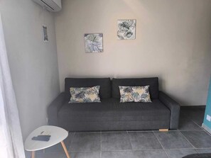 Een grijze bank met gekleurde kussens, een klein wit tafeltje en twee kunstwerken aan de muur.