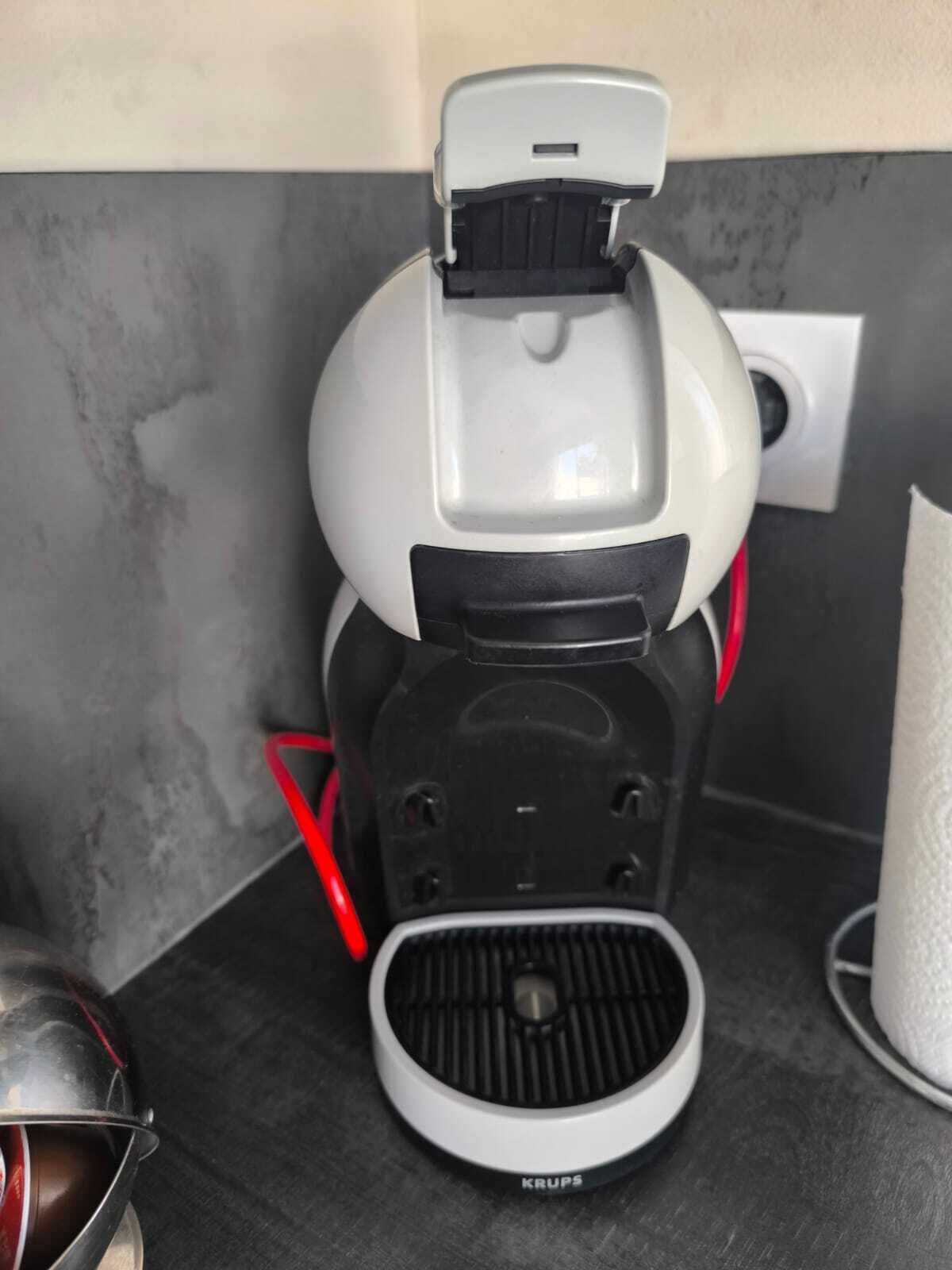 A coffee maker with a Krups brand label, a red cord, and a power outlet in the background.