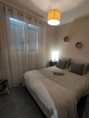 Een slaapkamer met een groot bed, gordijnen, een nachtkastje en een wandlamp.