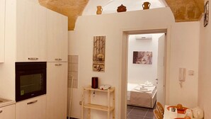 A compact kitchen with a built-in oven, a wooden shelf, and a dining area with a table and chairs. - Suite Carlotta Premium (Lecce)
