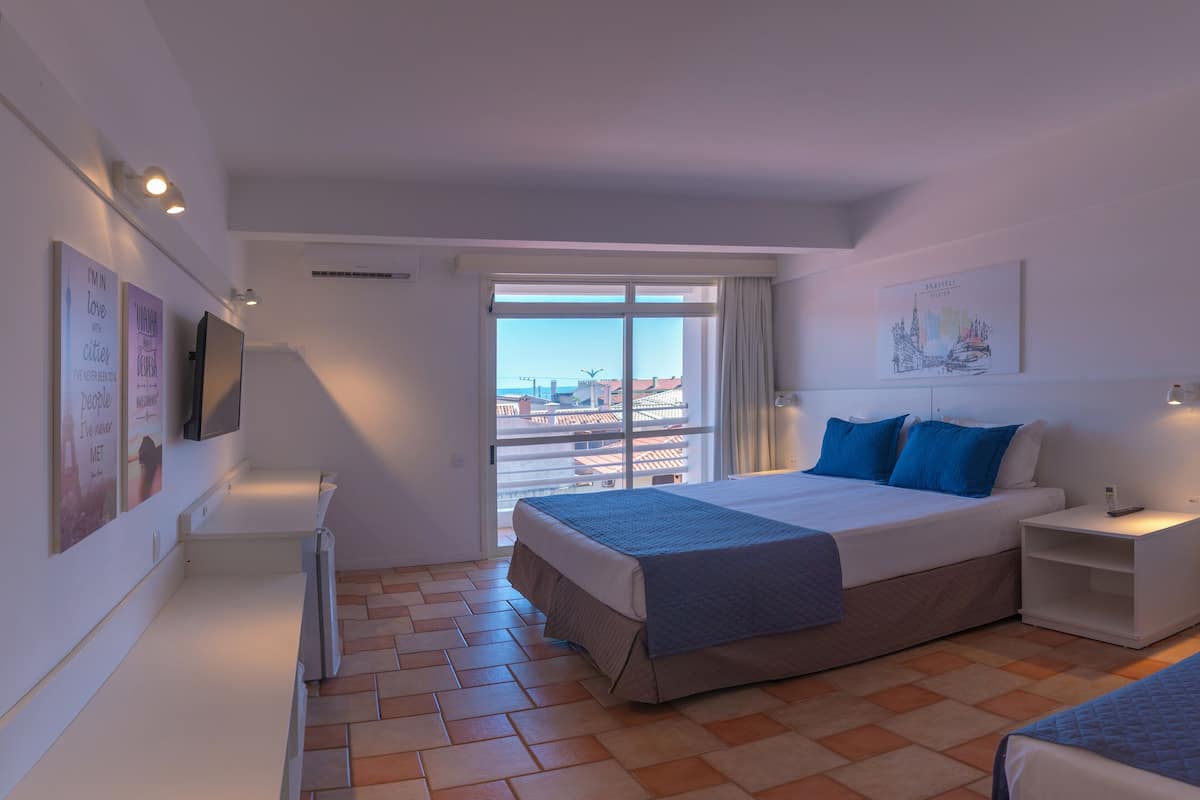 A hotel room with a large bed, a bedside table, a TV, and a window with a city view.