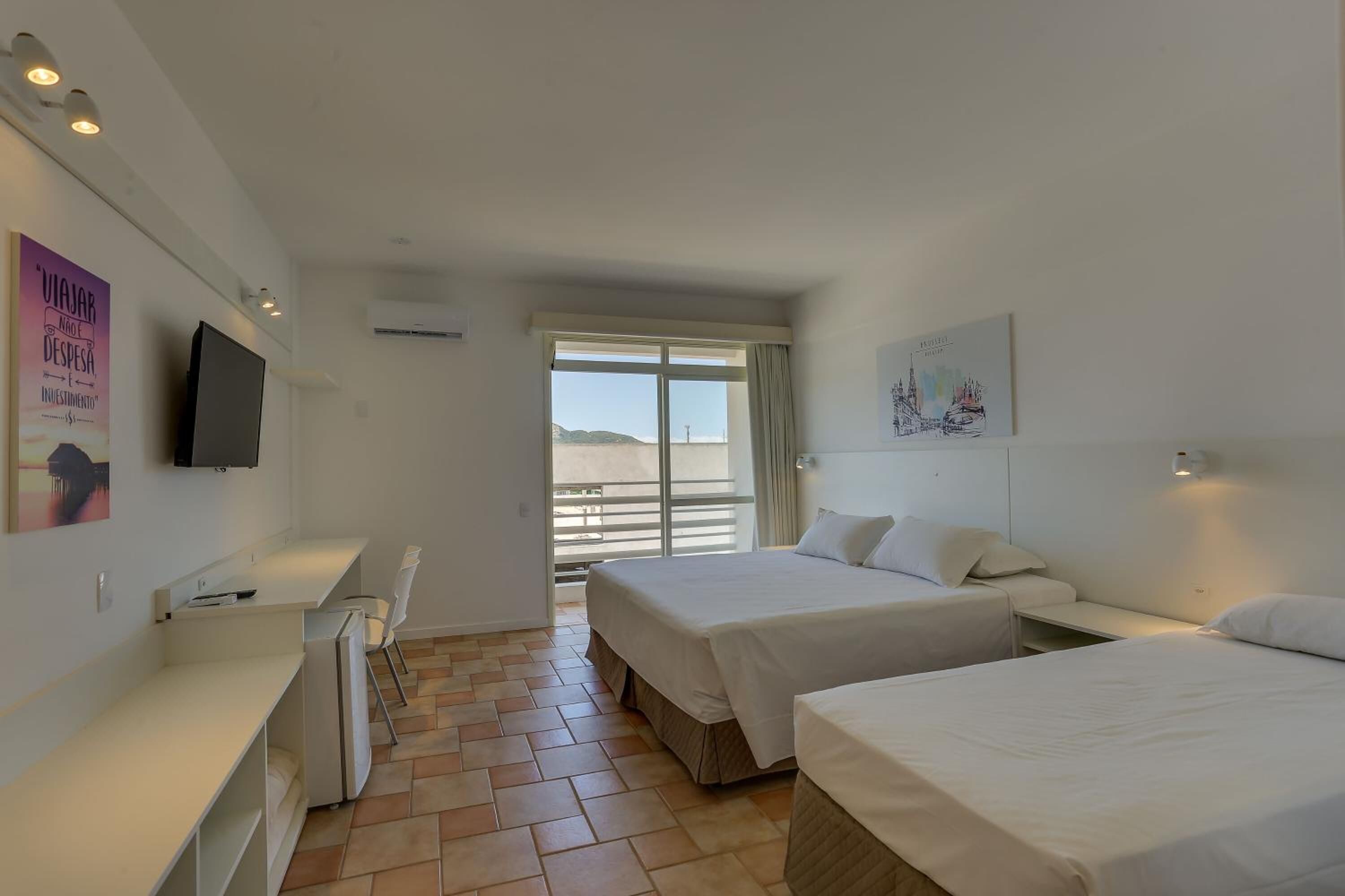 Habitación de hotel con dos camas, un escritorio, una silla, un televisor y un balcón con vistas.