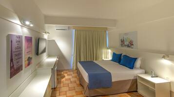 A hotel room with a bed, a bedside table, a TV, a window with curtains, and wall art.