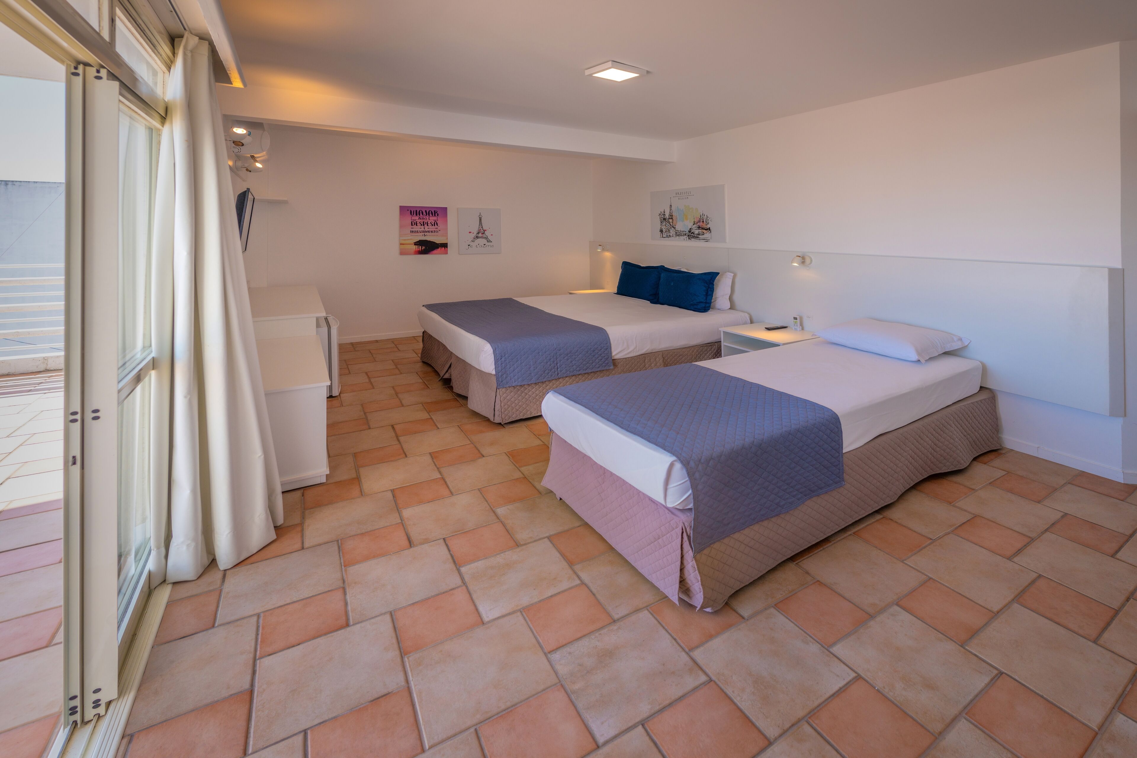 Una habitación de hotel con dos camas, un escritorio pequeño y una ventana con cortinas.