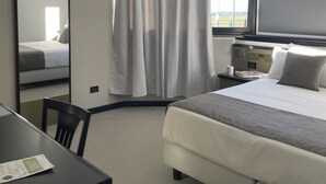 A hotel room with a bed, a desk, a chair, a mirror, and a window with curtains. - Hotel Gardenia Fiera (Cermenate)