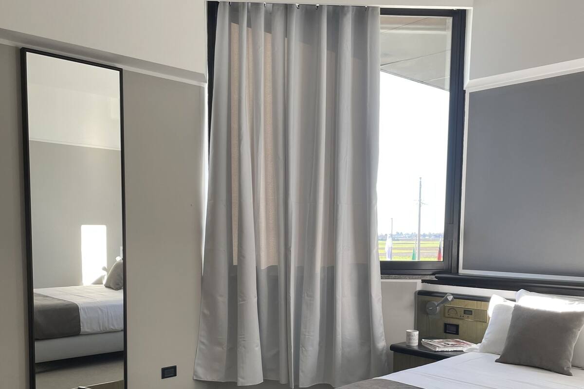 A hotel room with a bed, a desk, a chair, a mirror, and a window with curtains.