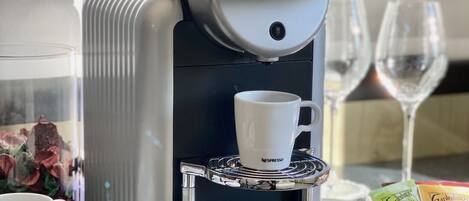 A Nespresso coffee machine with a cup holder, a glass of water, and a wine glass on a table.