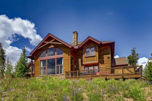 Une cabane en bois dotée de grandes fenêtres, d’une cheminée et d’une terrasse.