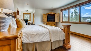 A bedroom with a bed, wooden cabinet, TV, and large windows.