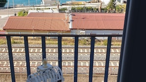 Ein Balkon mit weißem Tisch, einer Zierlaterne und Blick auf das Meer und die Berge.