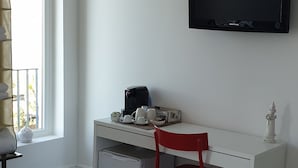 Ein weißer Schreibtisch, ein roter Sessel, ein kleiner, weißer Kühlschrank und ein schwarzer Fernseher an der Wand.