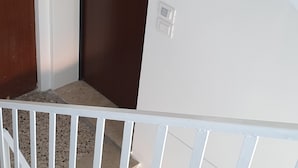 Eine Treppe mit weißen Geländern, einer dunkelbraunen Tür und einer weißen Wand mit einem Lichtschalter.