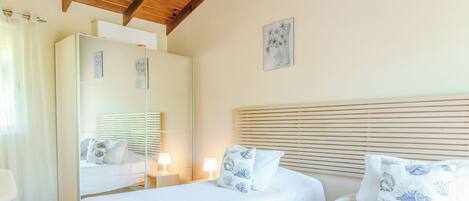 A bedroom with two beds, wooden ceiling beams, a large mirror, and a small bedside table with a lamp.