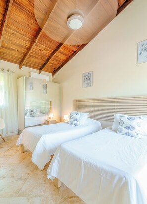 Quarto com duas camas, vigas de madeira no teto, um espelho grande e uma pequena mesa de cabeceira com abajur.