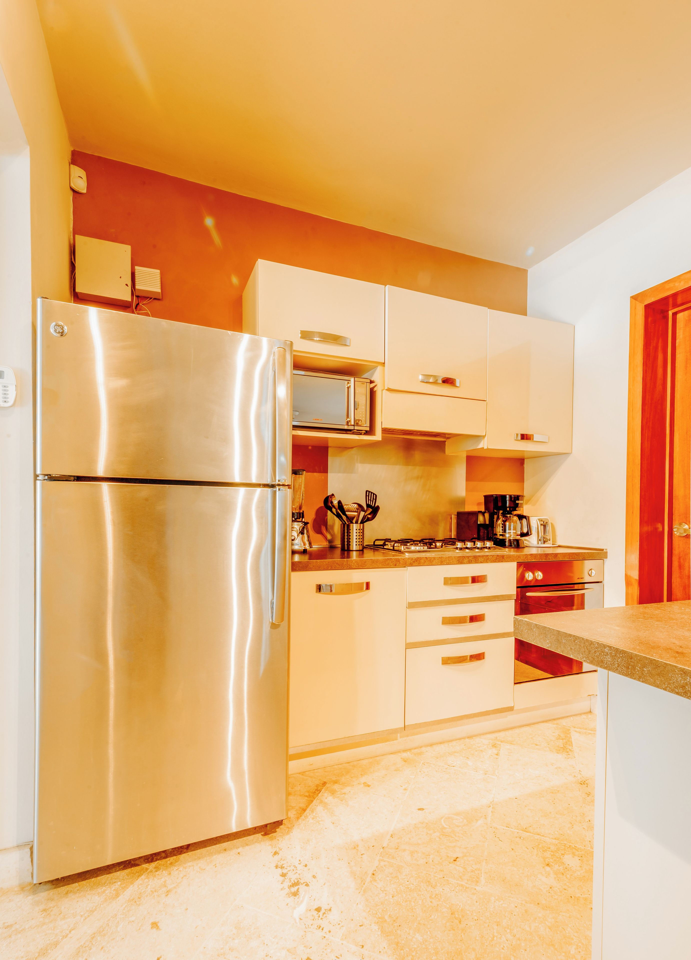 Una cocina compacta con electrodomésticos de acero inoxidable, armarios blancos y piso de baldosas.