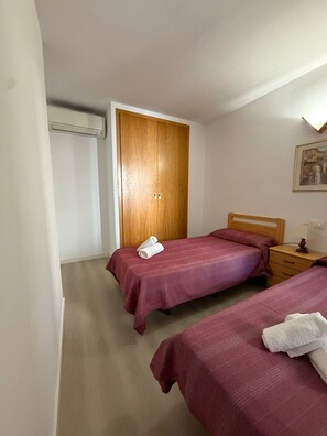 Ein Schlafzimmer mit zwei Betten, einem Holzschrank, einem Nachttisch und einer Wand-Klimaanlage.