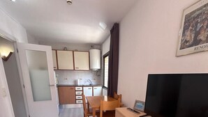 Un espacio habitable compacto con kitchenette, comedor y televisor sobre un mueble de madera.