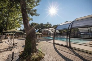 En træterrasse med swimmingpool, overdækkede siddeområder og et stort træ.