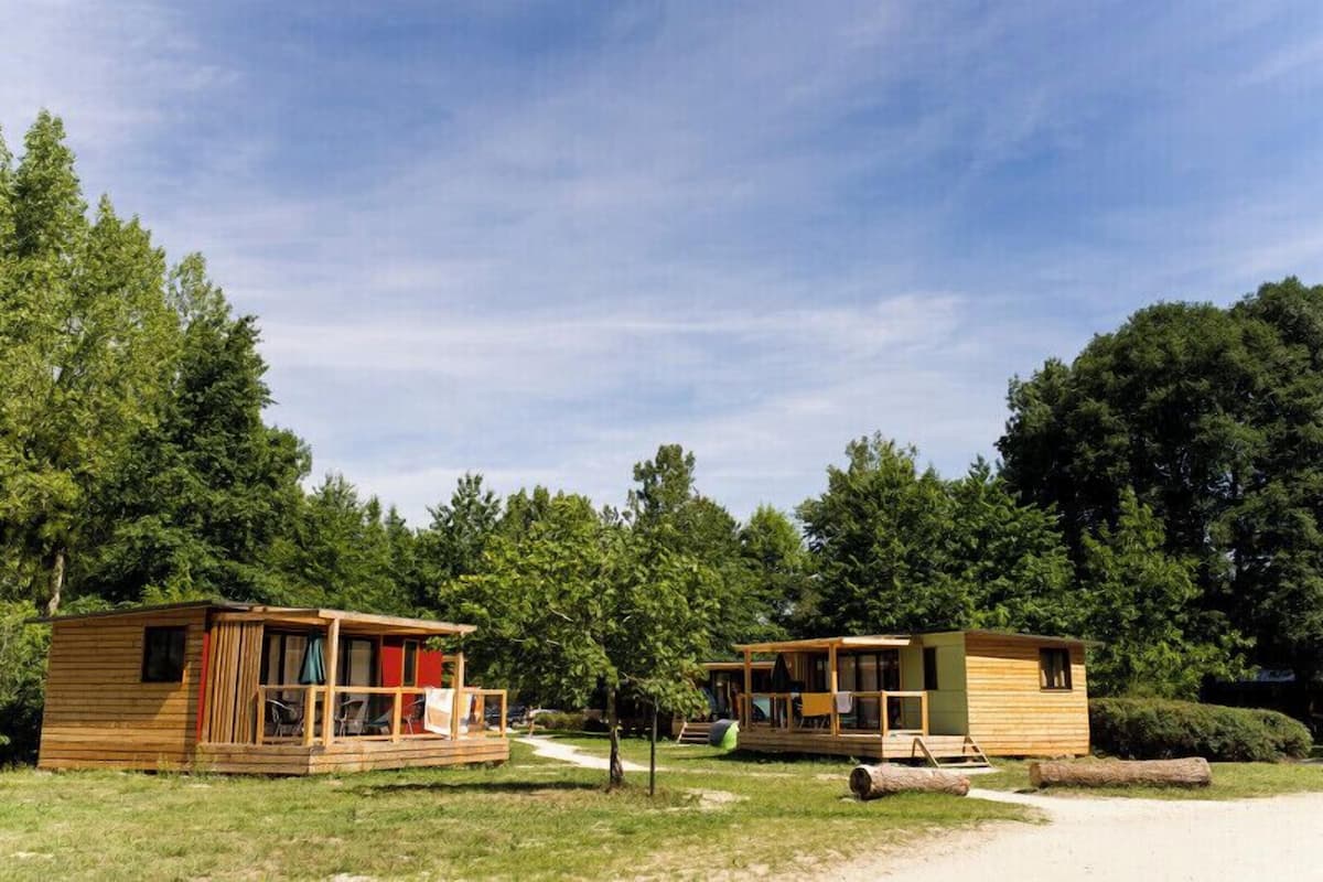 Deux cabanes en bois dotées de balcons, entourées d’arbres et baignées par un ciel dégagé.