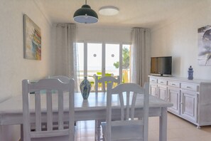 A dining area with a white table and chairs, a television on a cabinet, and a painting on the wall.