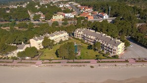 Eine Luftaufnahme eines Küstenhotels mit mehreren Gebäuden, einem Strand und einem Parkplatz.