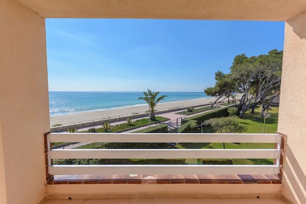 A balcony with a view of a beach and a well-maintained garden.